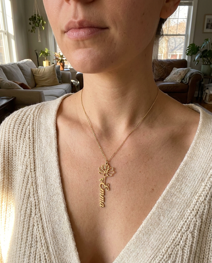 Woman in a cream knit sweater wearing the gold-tone Emma flower pendant at her collarbone in a softly lit living room