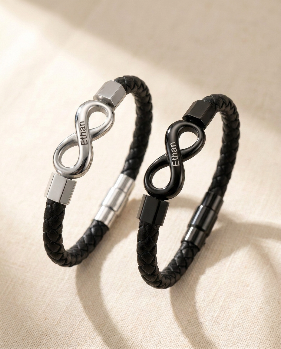 Two braided cord bracelets side by side on cream linen, one with a steel-tone infinity link and one with a black link, both engraved Ethan
