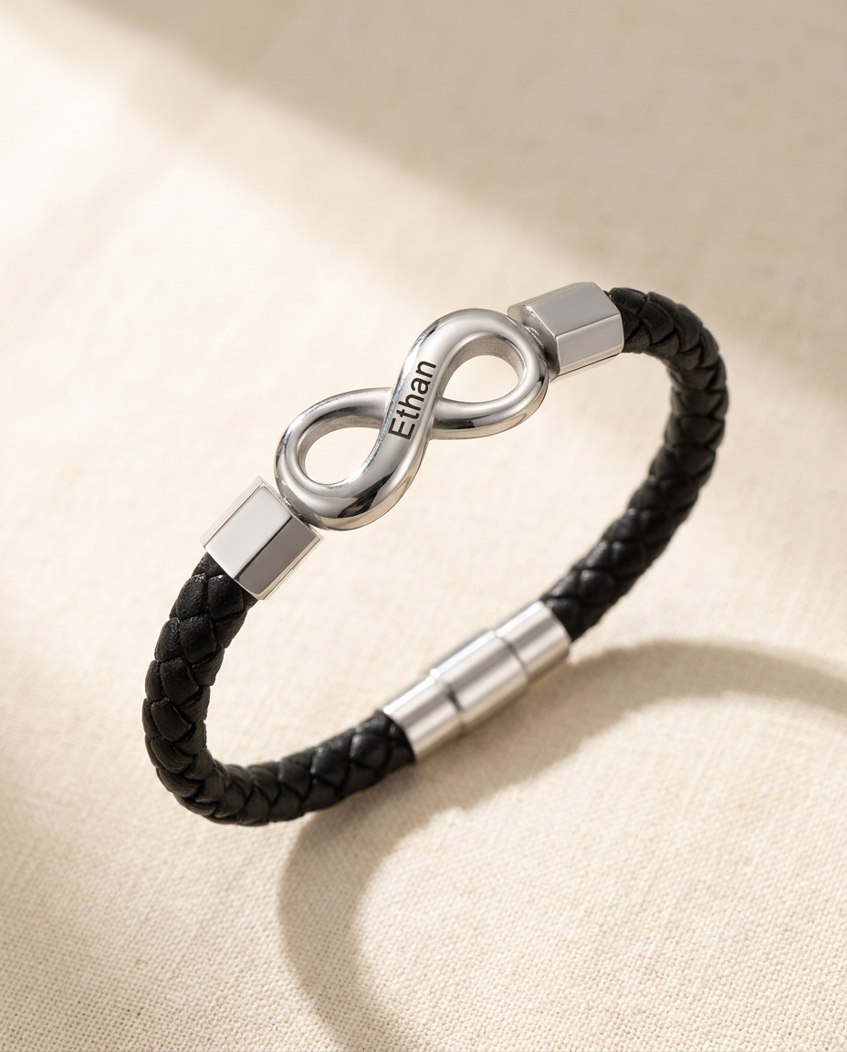 Braided cord bracelet with a steel-tone infinity link engraved Ethan, lying in an open curve on cream linen in soft window light