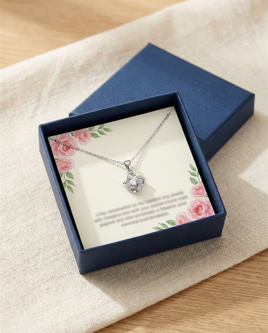 Open navy gift box with a printed card and a silver-tone knot pendant necklace with a clear center stone